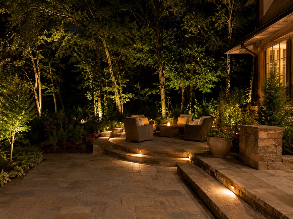Statesville backyard patio, firepit and trees lit at night with warm low-voltage outdoor-living lighting (design concept)