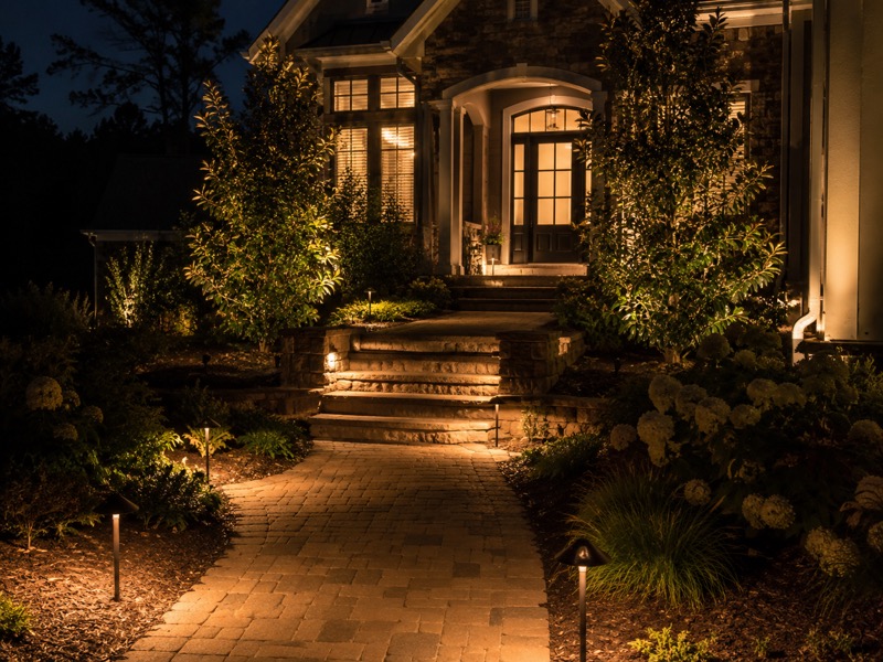 New-construction Troutman home facade with architectural uplighting on columns and trees at night (design concept)